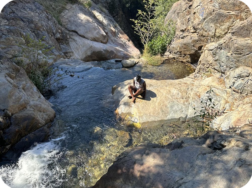 A person sitting on a rock beside a creek and small waterfall